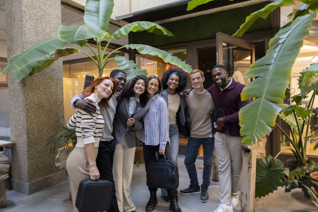 Empresarios multiétnicos abrazándose, sonriendo y luciendo felices en su moderna oficina de coworking con grandes plantas tropicales